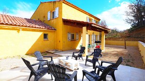 A yellow building with a tiled roof and a patio area with black chairs and a table.
