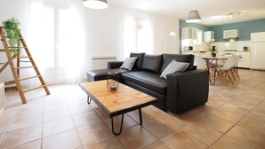 A modern living room with a black sofa, a wooden coffee table, and a kitchen in the background.