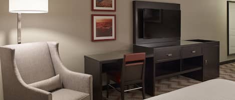A hotel room with a bed, a desk, a chair, a TV, and two framed pictures on the wall.