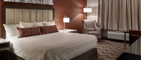Une chambre d’hôtel avec un grand lit, une tête de lit, une table de chevet, une chaise, une lampe, une fenêtre avec des rideaux et une œuvre d’art murale.