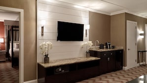 A hotel room with a large flat-screen TV mounted on the wall, a dark wooden cabinet with a built-in sink, and a patterned carpet. - Oxford Casino Hotel (Oxford)