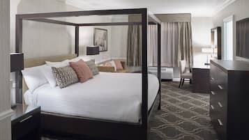 A four-poster bed with a canopy, a desk with a lamp, a chair, and a television on a dresser.