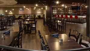 A restaurant with multiple dining tables and chairs, an American flag on the wall, and a bar area with red chairs. - Oxford Casino Hotel (Oxford)