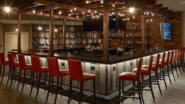A bar area with a long counter, red bar stools, and a brick wall with a menu board. - Oxford Casino Hotel (Oxford)