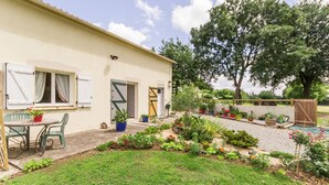 Une maison avec un jardin, une terrasse avec des chaises et une clôture en bois.