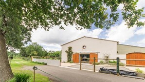 Un bâtiment avec une grande porte ouverte, une zone délimitée par une clôture et un arbre au premier plan.