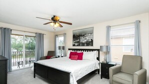 A bedroom with a bed, a chair, a nightstand, a ceiling fan, and a window with curtains.