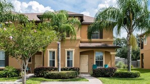 A two-story residential building with a beige facade, a front entrance, and a paved driveway.
