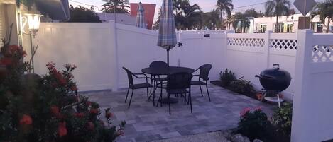 A patio area with a table and chairs, a barbecue grill, and a white fence.