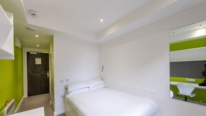 A hotel room with a bed, a bathroom mirror, and a door leading to another room. - University of Bath City Accommodation (Bath)
