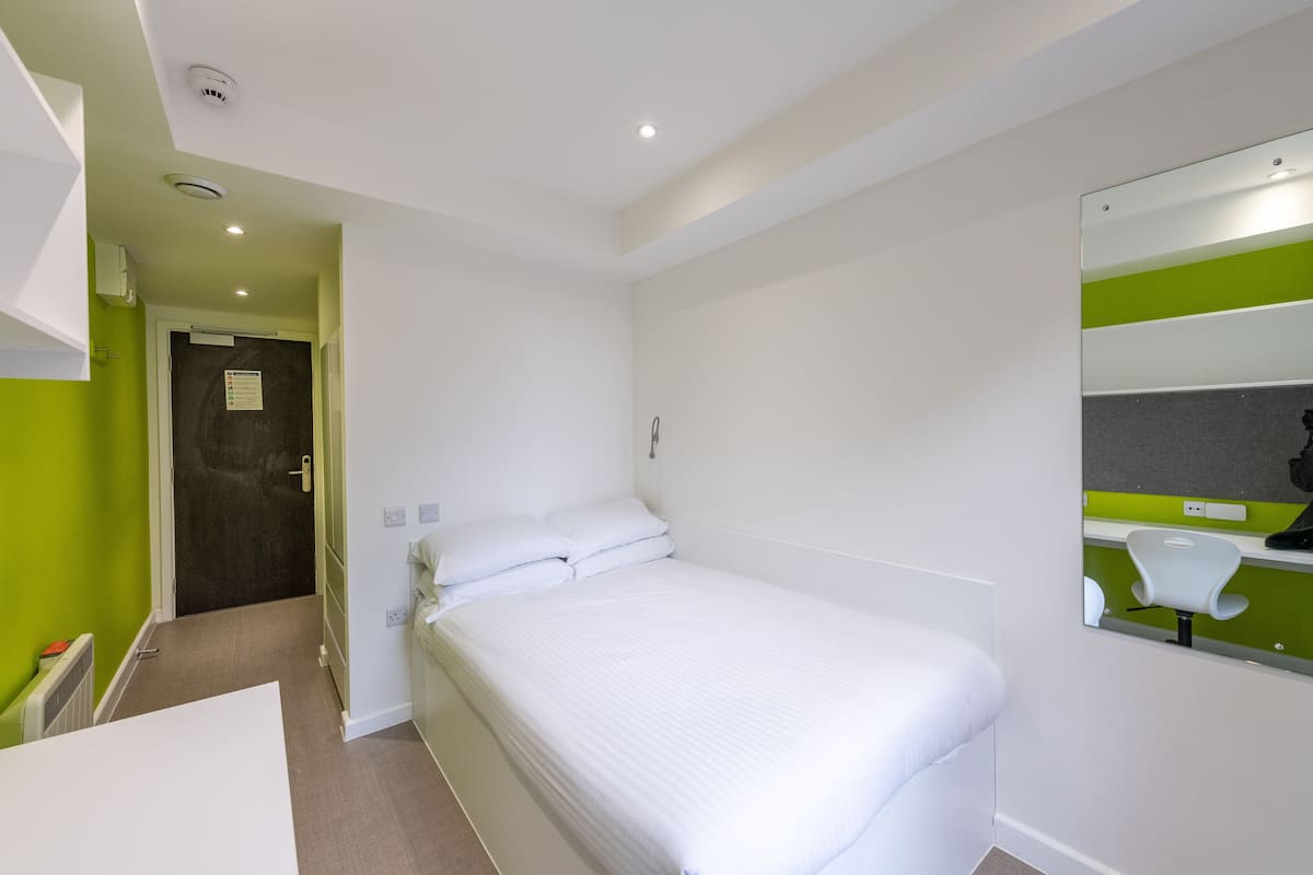 Quarto de hotel com cama, espelho de banheiro e porta que dá para outro cômodo.