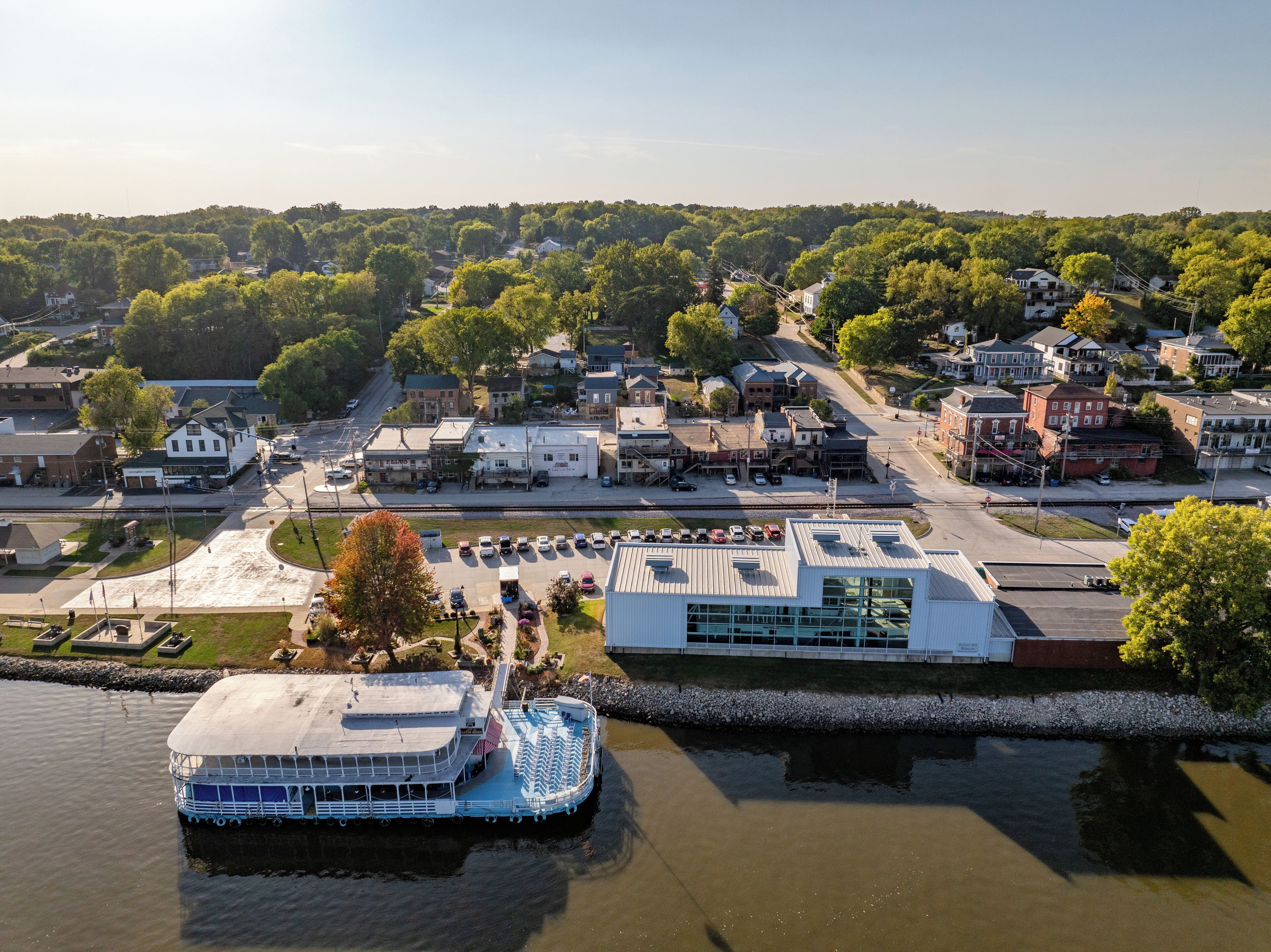 A riverfront town with a large white building, a docked boat, and a mix of residential and commercial buildings.