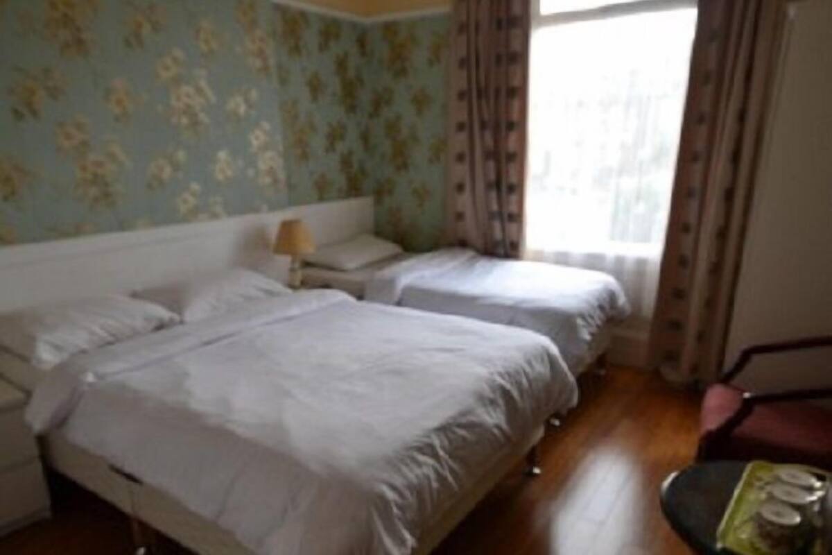 A room with two beds, a nightstand, a lamp, a chair, and a window with curtains.