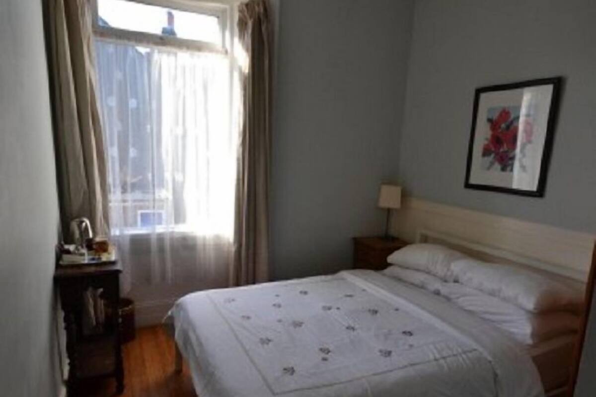 A bedroom with a bed, a nightstand, a lamp, and a window with curtains.