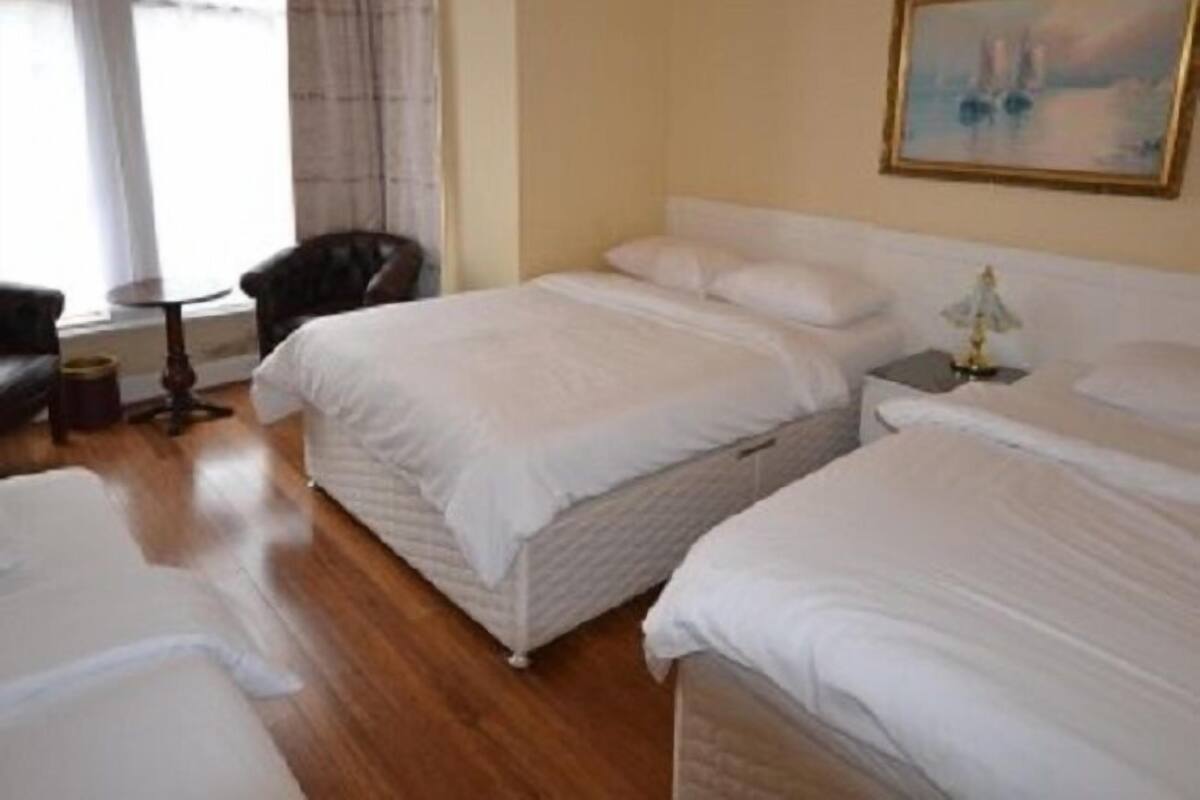 A hotel room with two beds, a chair, a small table, and a painting on the wall.