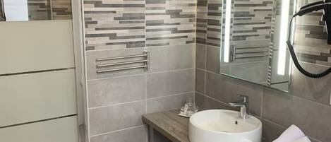 A modern bathroom with a glass shower enclosure, a wooden vanity with a sink, and a towel rack.