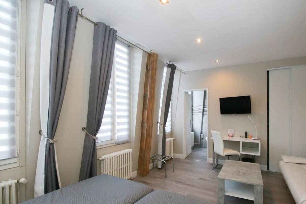 A modern, well-lit room with a bed, a white sofa, a small table, and a TV mounted on the wall.