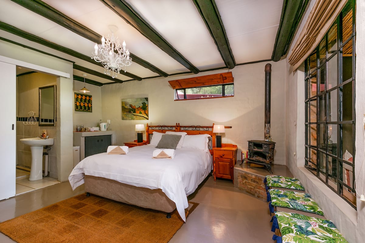Un dormitorio con una cama grande, mesitas de noche, una araña, una ventana con contraventanas y un cuadro en la pared.