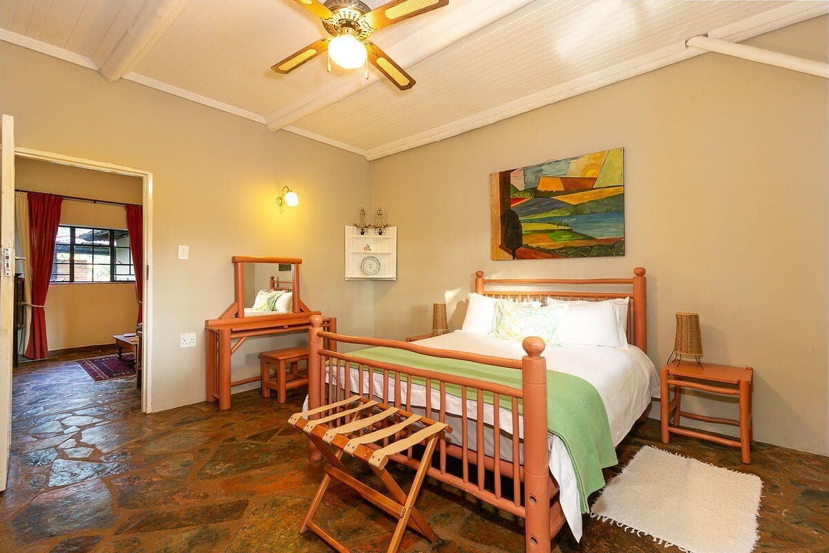 Un dormitorio con cama de madera, mesita de noche, cómoda, mecedora, un cuadro en la pared y ventilador de techo.