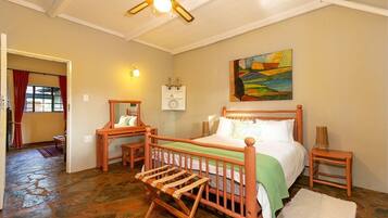 Un dormitorio con cama de madera, mesita de noche, cómoda, mecedora, un cuadro en la pared y ventilador de techo.