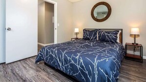 Un dormitorio con una cama, dos mesitas de noche, un tocador, un espejo y una puerta.