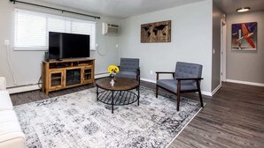 Una sala de estar con televisor, dos sillones, una mesita de centro y un tapete estampado.