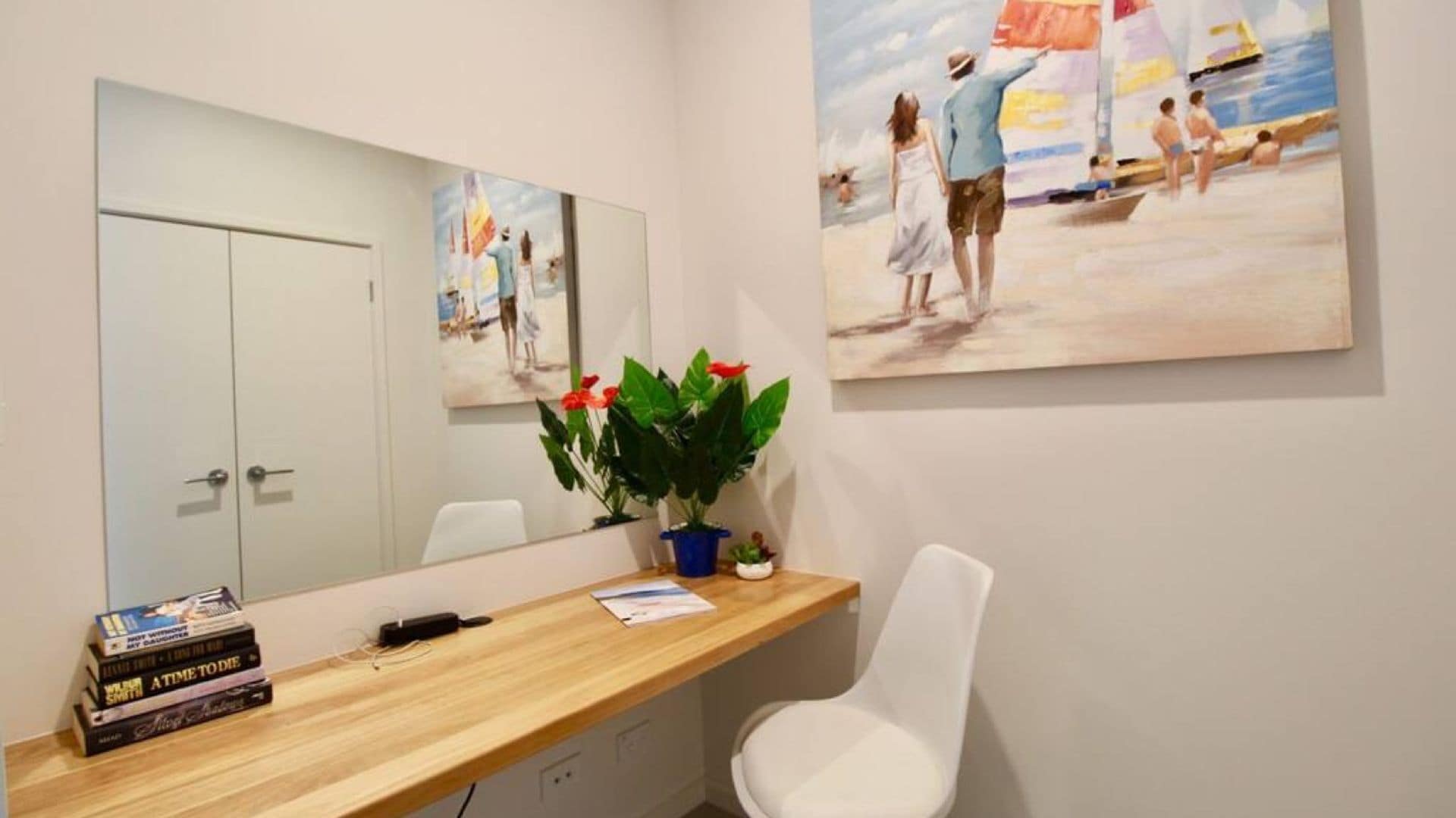 Ein Zimmer mit einem Holztisch, einem weißen Stuhl, einem Spiegel und zwei Bildern an der Wand.