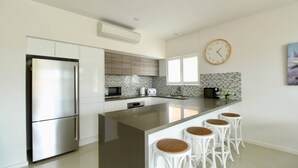 A modern kitchen with a central island, stainless steel appliances, and a clock on the wall. - Avalon Apartment by Book Jervis Bay (Huskisson)