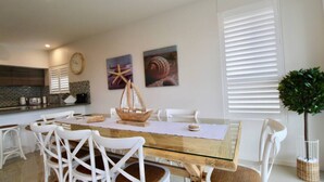 A dining area with a glass-top table, white chairs, and a wooden boat centerpiece. - Avalon Apartment by Book Jervis Bay (Huskisson)
