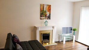 Ein modernes Wohnzimmer mit Kamin, einer Couch, einem Fernseher auf einem Glastisch und einem Bild an der Wand.