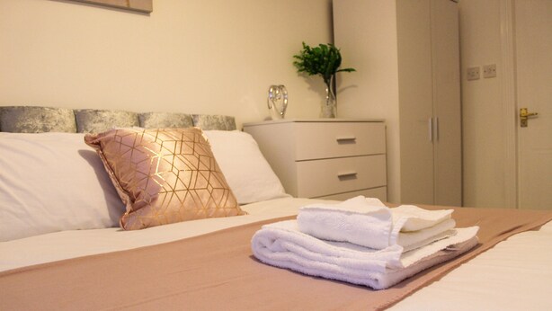 Ein ordentlich gemachtes Bett mit einer braunen Tagesdecke, weißen Kissen und einem gefalteten weißen Handtuch.