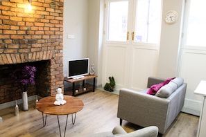 A living room with a brick fireplace, a flat-screen TV on a stand, a grey sofa, and a small round table. - The Coffee Cup (Liverpool)