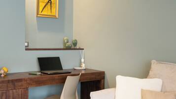 A room with a desk, chair, laptop, and a couch with pillows.