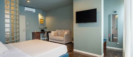 A modern bedroom with a bed, a desk, a sofa, a TV, and a bathroom mirror.