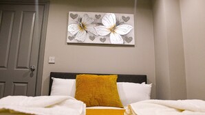 A hotel room with a bed, a yellow pillow, white pillows, and a painting of flowers on the wall. - Ropewalks Retreat (Liverpool)