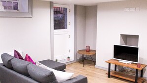 A living room with a grey sofa, a small wooden table with a TV, and a door with a view of a balcony. - Ropewalks Retreat (Liverpool)