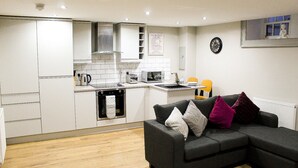 A compact living space with a kitchenette, a sofa with cushions, and a clock on the wall. - Ropewalks Retreat (Liverpool)