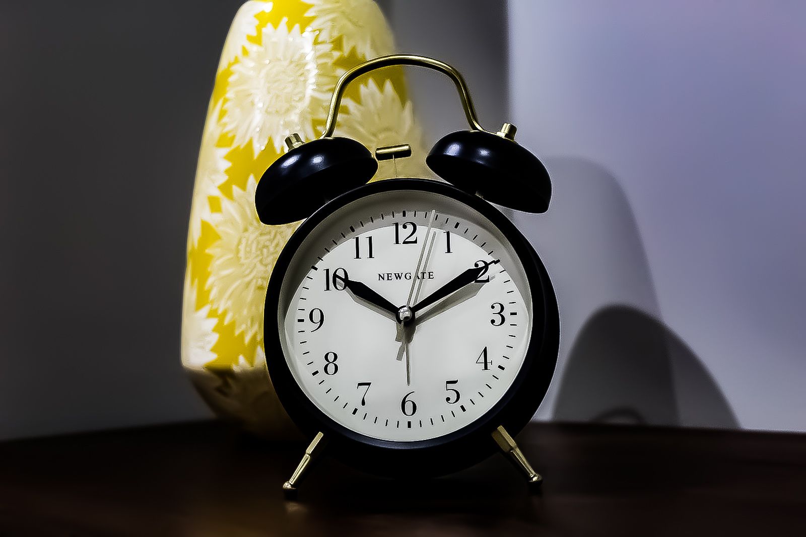 A black alarm clock with a white face and black numbers, placed on a wooden surface.