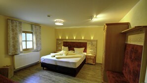 Un dormitorio con cama, mesitas de noche, radiador, ventana con cortinas y armario.