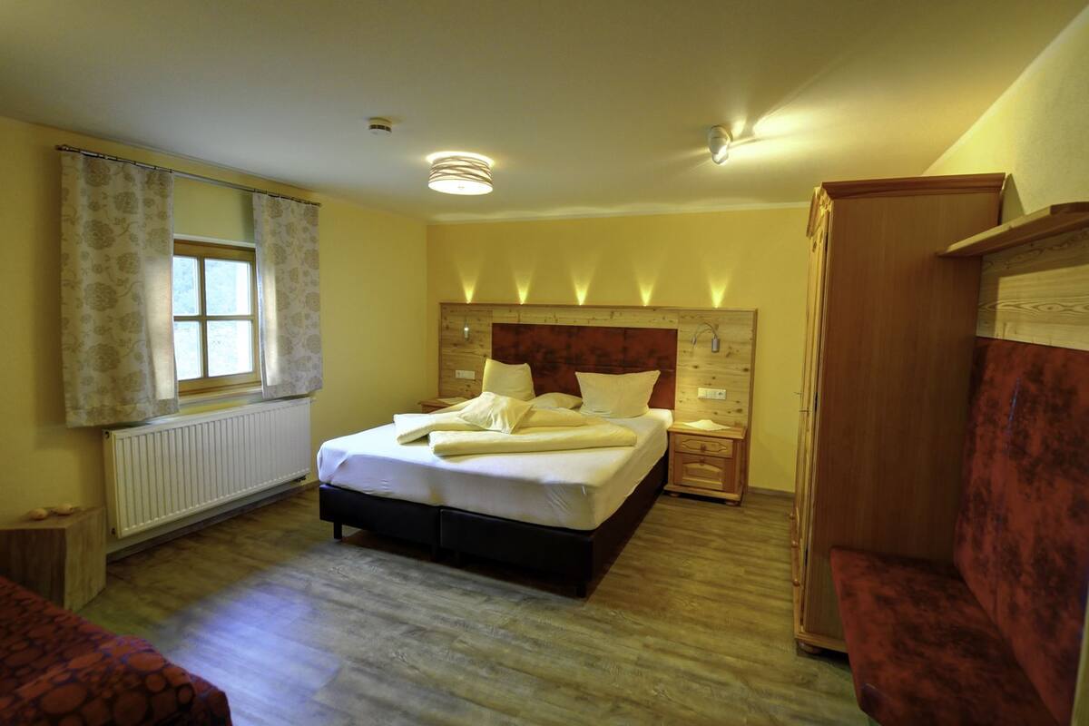 A bedroom with a bed, bedside tables, a radiator, a window with curtains, and a wardrobe.