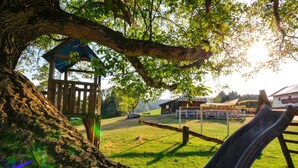 Un parque infantil con un tobogán, una casita de madera y una zona vallada.