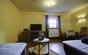 A cozy living room with a television, wooden furniture, a small table with a vase, and a window with curtains.