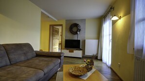Una sala de estar con un sofá, un televisor, una corona decorativa en la pared y una ventana con cortinas.