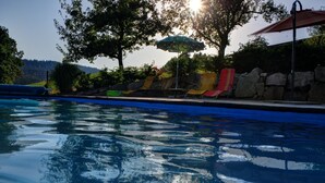 Una piscina con vista despejada al agua, rodeada de sillones de descanso y una zona sombreada.