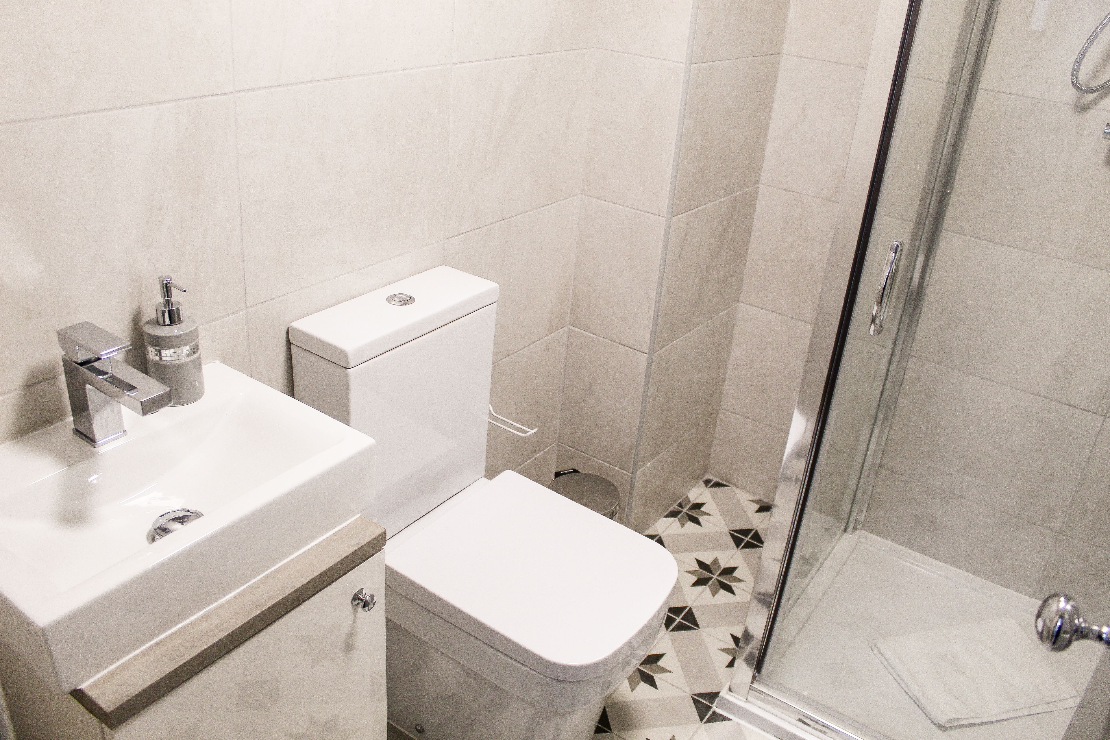 Ein Badezimmer mit Toilette, Waschbecken inklusive Seifenspender und Duschbereich mit Glastür.