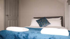Un lit bien fait, avec une couverture bleue et un coussin à motifs géométriques, une porte blanche et un mur blanc.