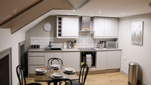 Une cuisine compacte avec des meubles blancs, un four à micro-ondes, une bouilloire et une horloge au mur.