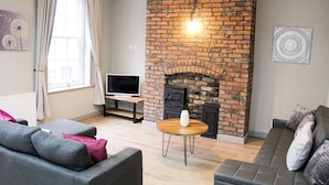 A living room with a brick fireplace, a sofa, a television, and a dining table. - Mersey Place (Liverpool)