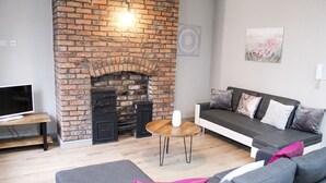 A living room with a brick fireplace, a sofa, a TV on a stand, and a small wooden table. - Mersey Place (Liverpool)