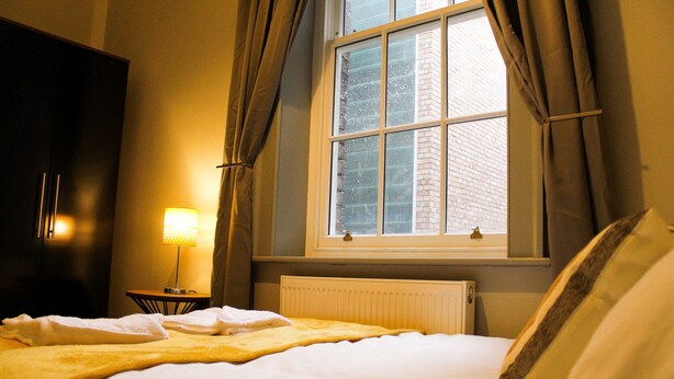 A hotel room with a bed, a lamp, a window with curtains, and a radiator. - Mersey Place (Liverpool)